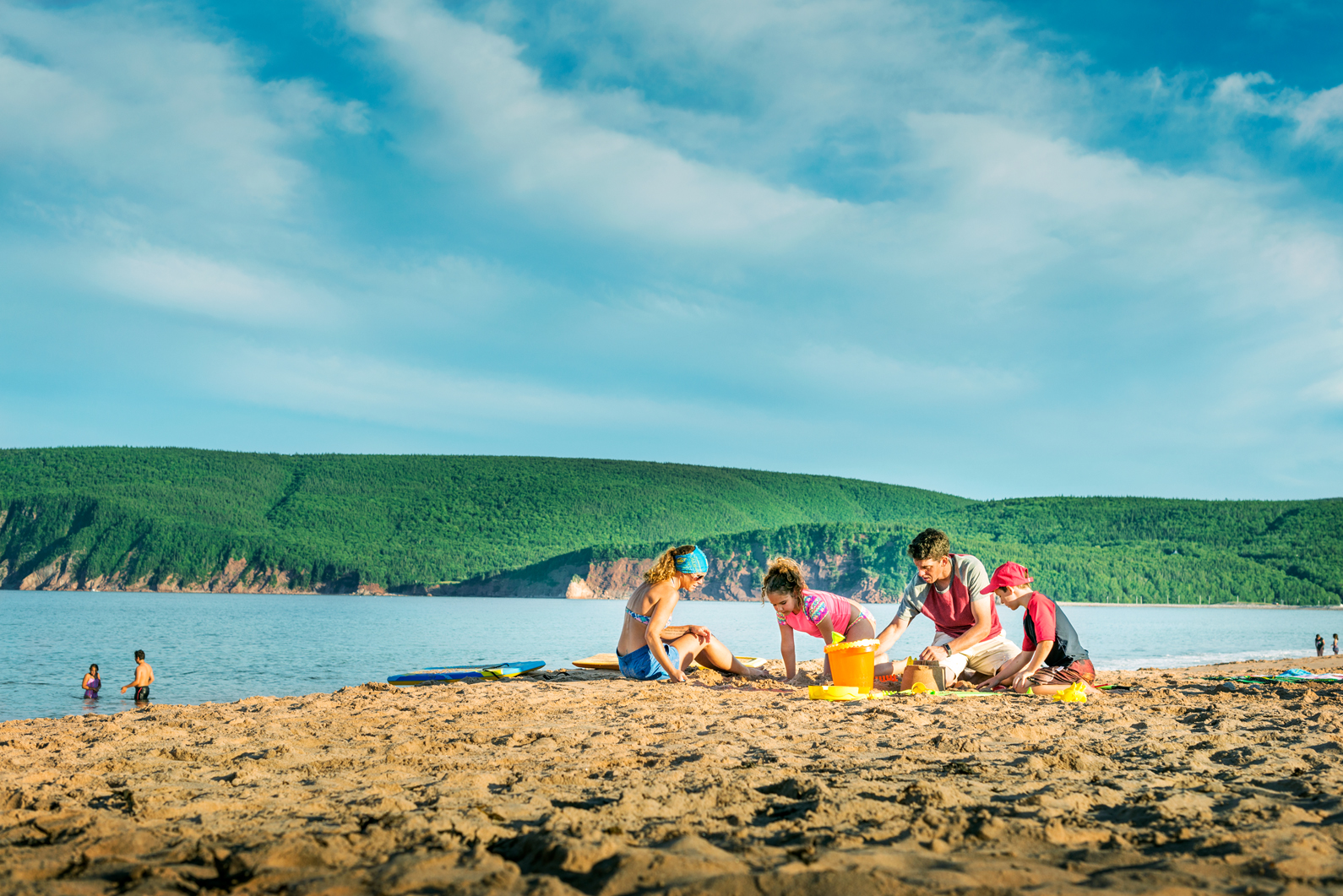 Family playing in the sand at Ingonish Beach with Cape Breton Highlands in the background
