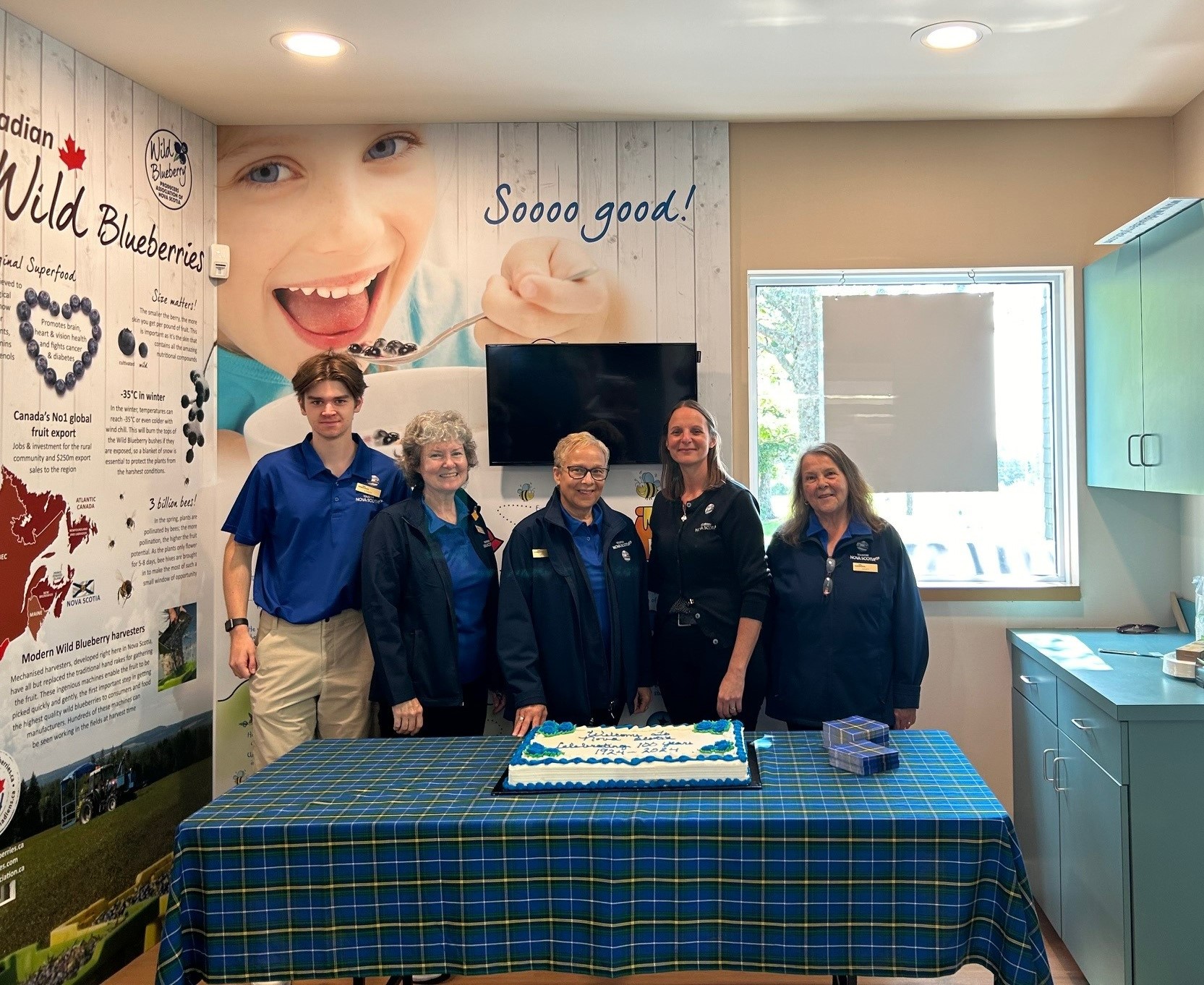 Five people standing behind a table with a white square cake on top of it