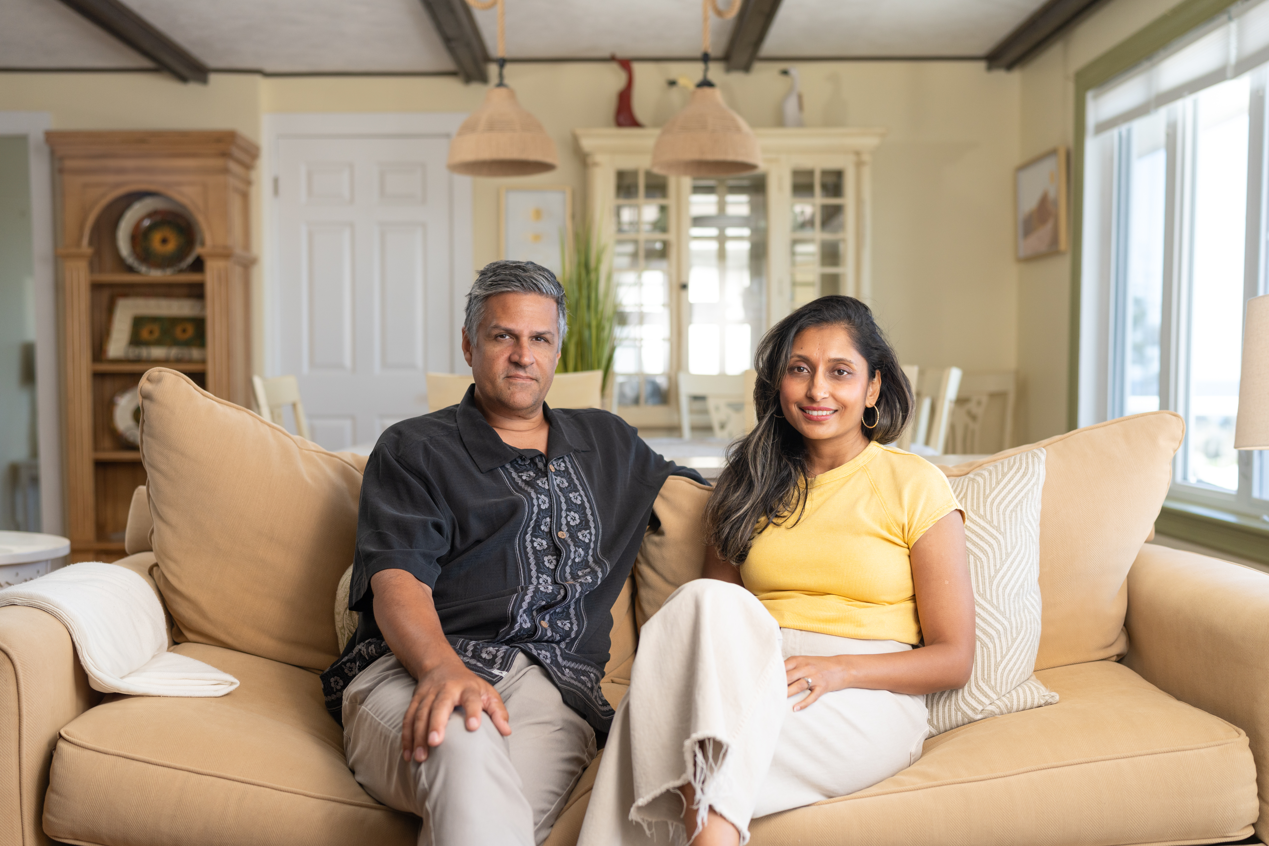 Two people sitting inside on a tan coach 