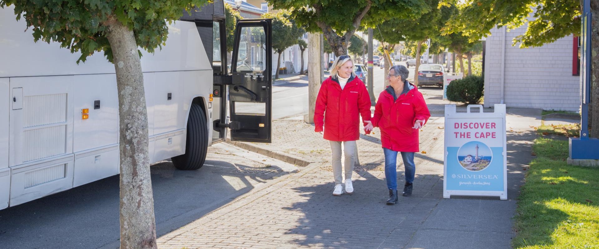 Two people taking part in a tour standing next to their tour bus.