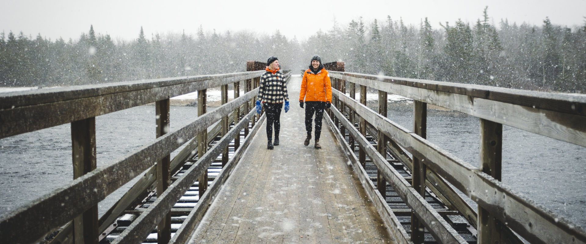 Two people walking in the snow on a boardwalk bridge. 