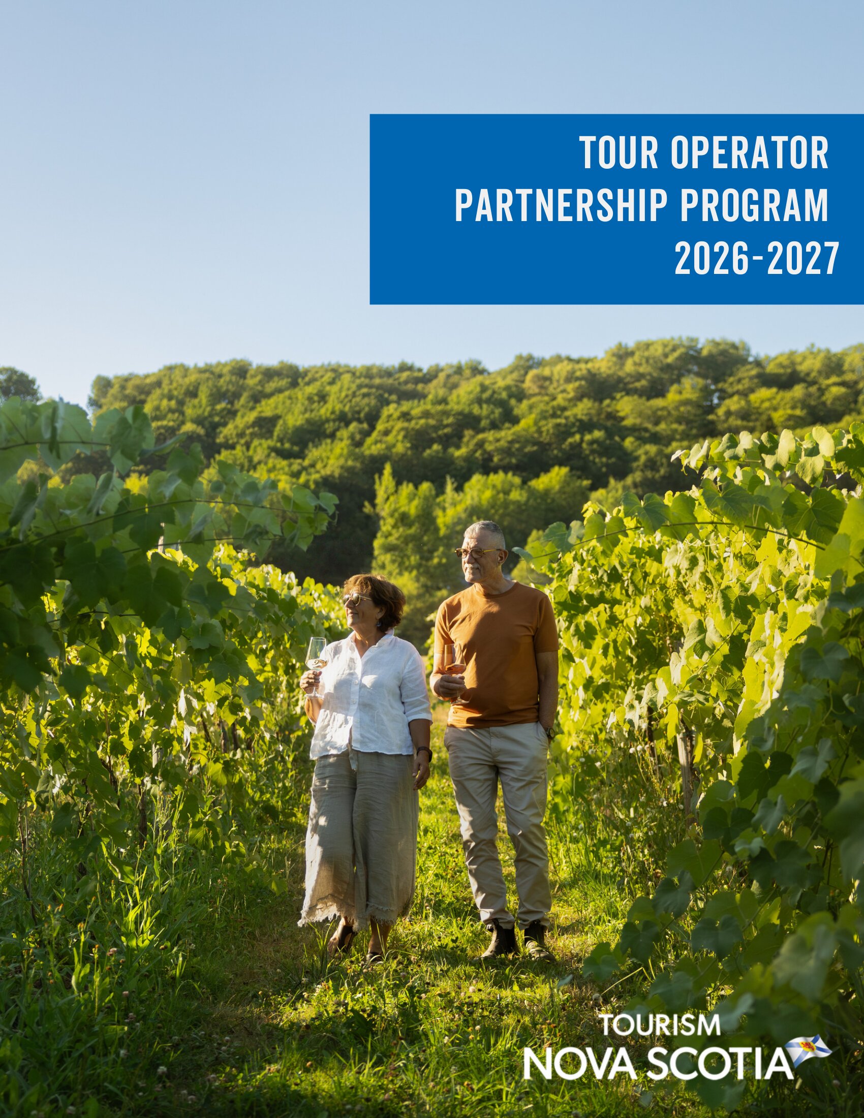 Two people walking in a green vineyard holding a glass of wine