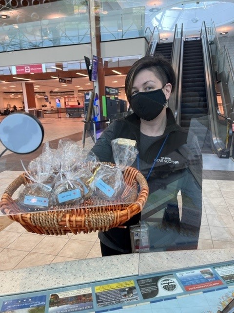 Woman in Nova Scotia uniform holding a basket of cookies at the Halifax International Airport visitor information cetnre.