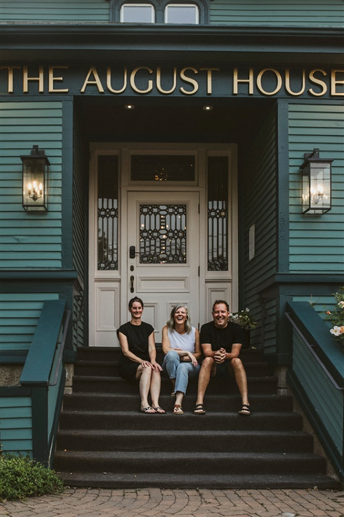 The three owners of The August House sit on the front porch steps. 