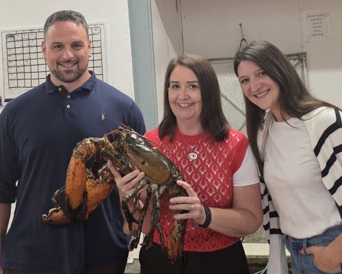 Three people standing together. The person in the middle is holding up a 11.5 pound lobster. 