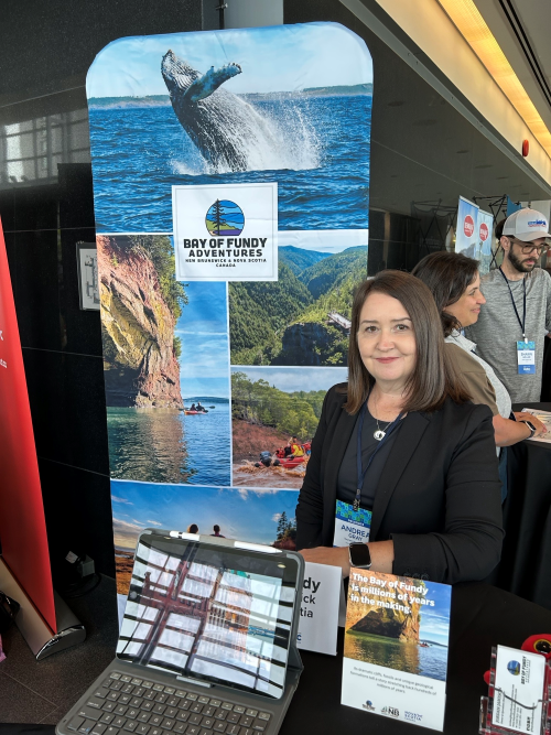 Andrea Gray seated next to a banner for Bay of Fundy Adventure Tours. 