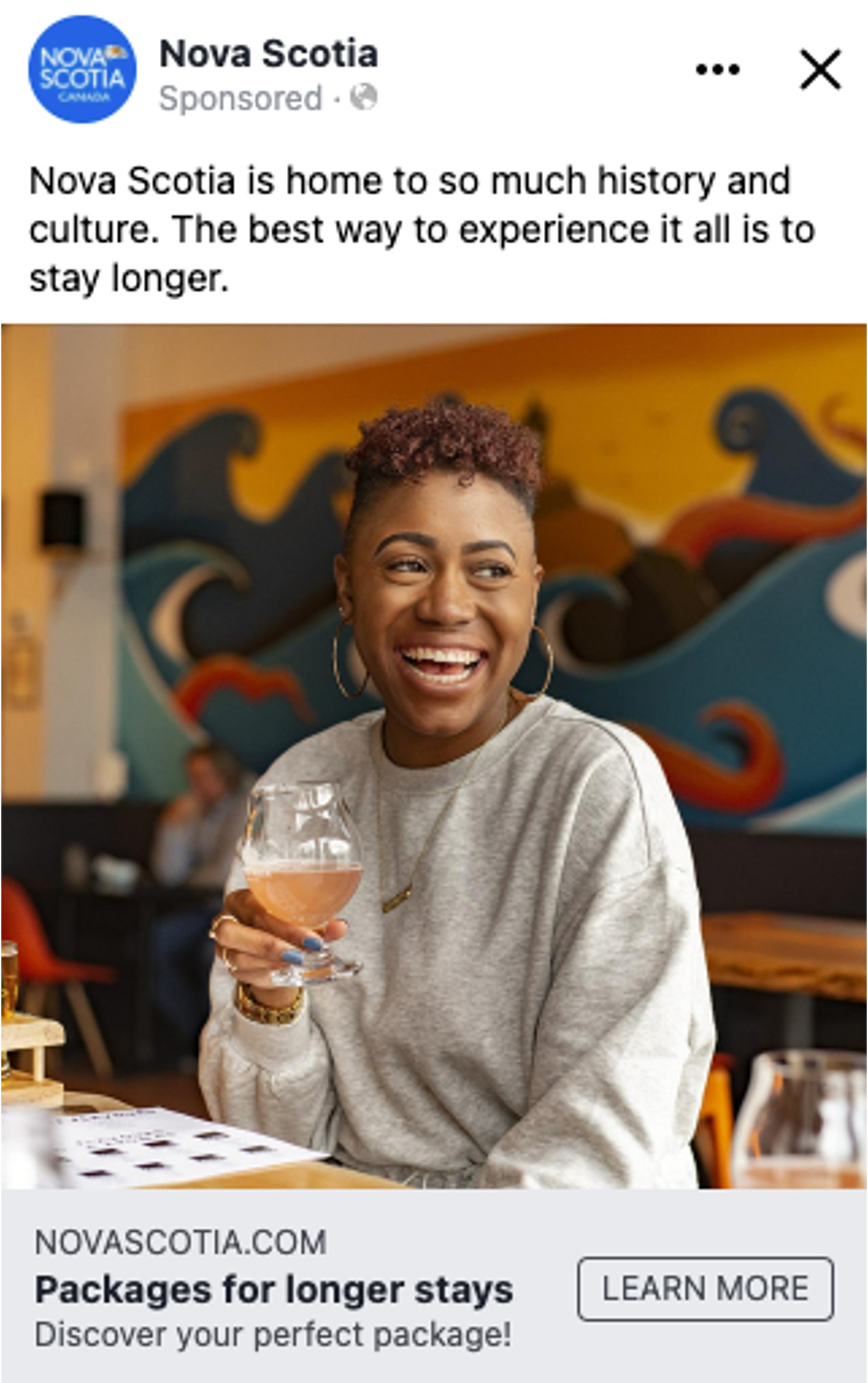 Screen shot of a Facebook ad on the Nova Scotia page. Image is a woman smiling and holding a glass of beer.