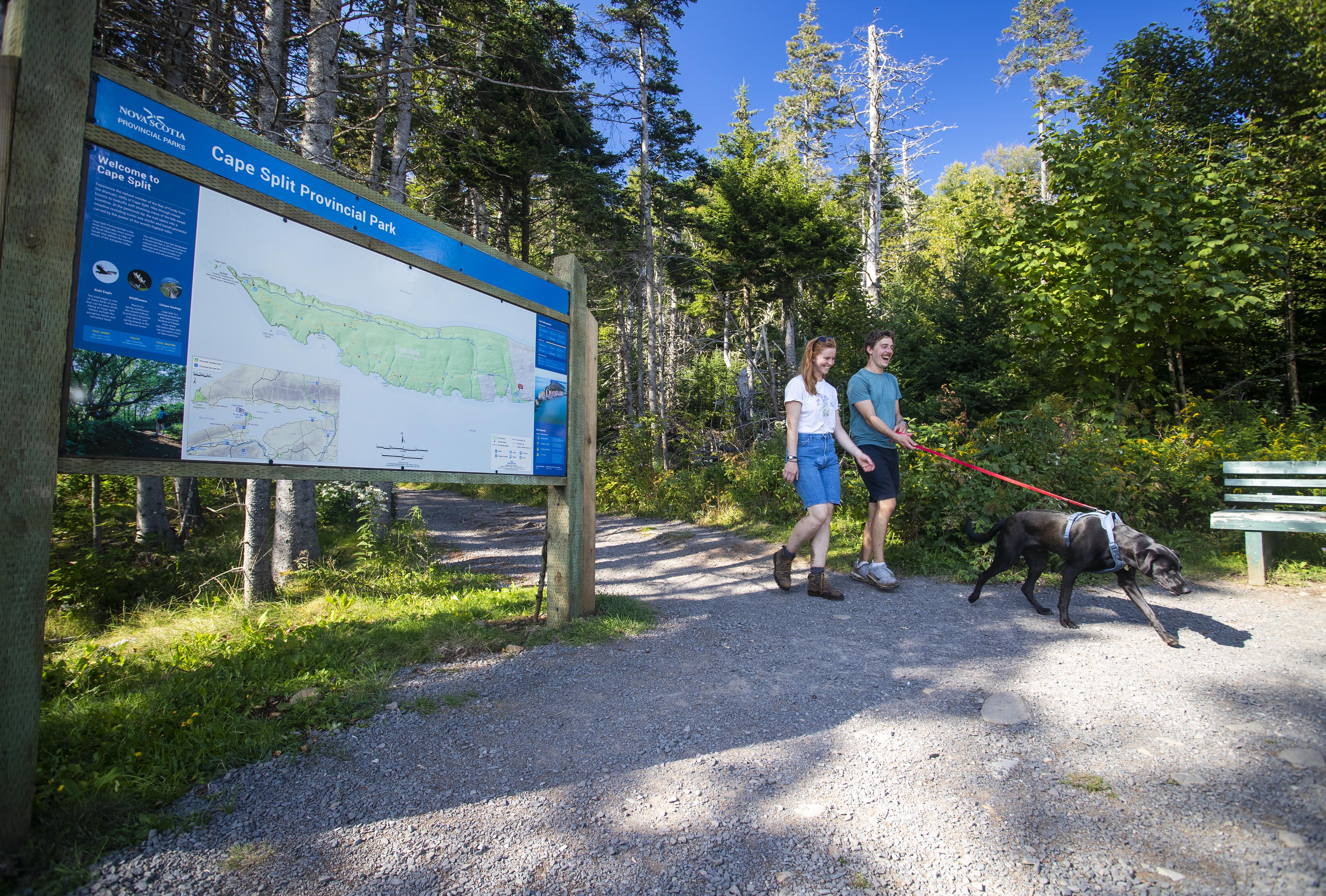 A man and woman walk their dog past the new trailhead sign at Cape Split.