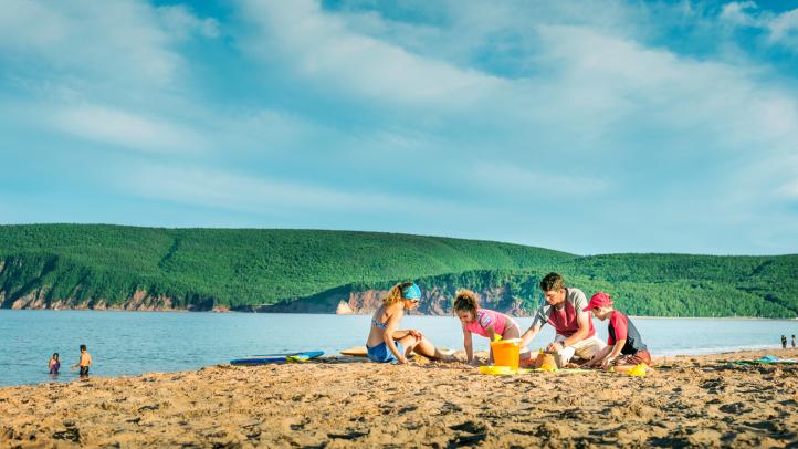Family playing in the sand at Ingonish Beach with Cape Breton Highlands in the background