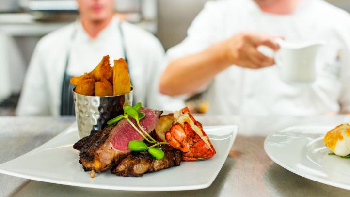 Plate of food on a counter with chefs in the background.