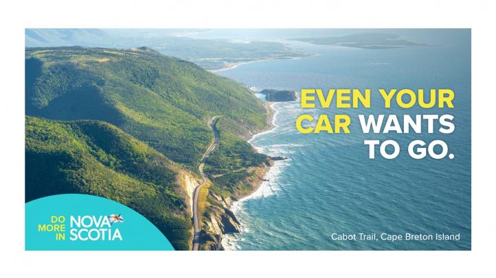 Image of road winding between the coast and mountains in Cape Breton Highlands. Text reads: Even your car wants to go.