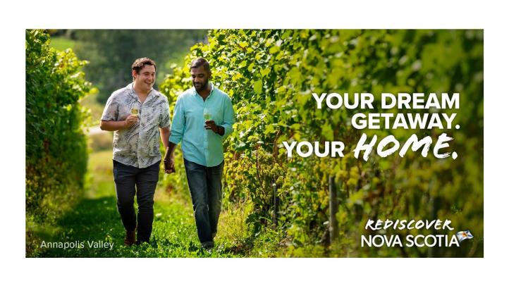 Image of two men holding hands walking through a vineyard. Text reads: Your dream getaway. Your home. Rediscover Nova Scotia.