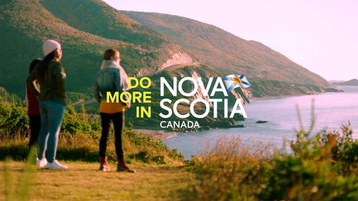 Three woman stand near the coast overlooking the Cabot Trail with fall leaf colours. Text reads: Do More in Nova Scotia Canada.