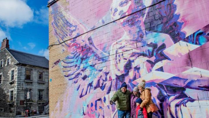 A family of four stands in front a mural on the side of a building.