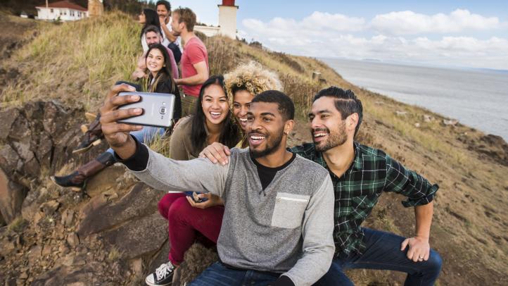Group of people taking a selfie on the cliff at Cape d'Or with the lighthouse in the background.