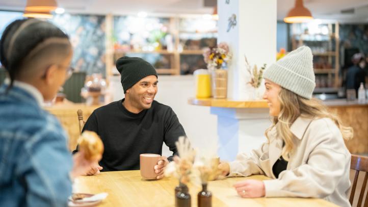 Three people sitting at a restaurant table, two wearing winter hats