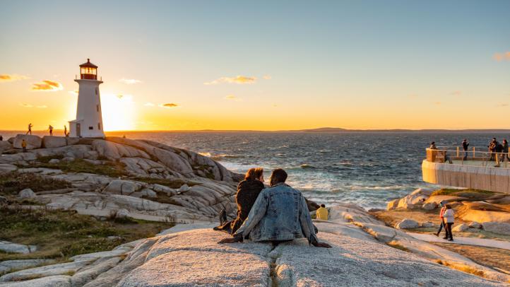 Two people back to sitting on a big rock overlooking the Peggy's Cove lighthouse and ocean