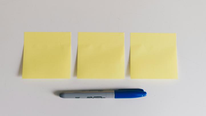 Three empty post-it notes on a surface with a blue sharpie marker underneath.