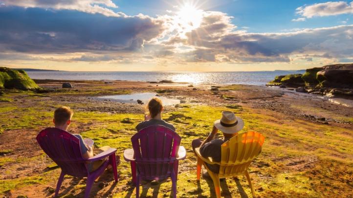 Three people in Adirondack chairs looking out over the ocean at Burntcoat Head Provincial Park. 