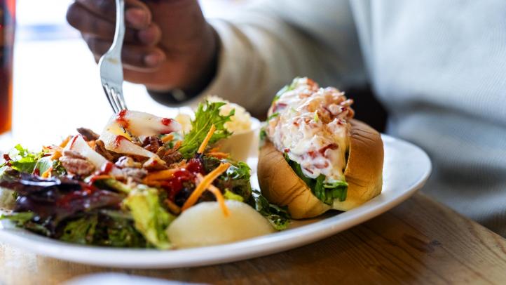 A person sitting at a table with fork in hand, digging into a lobster roll dinner. 