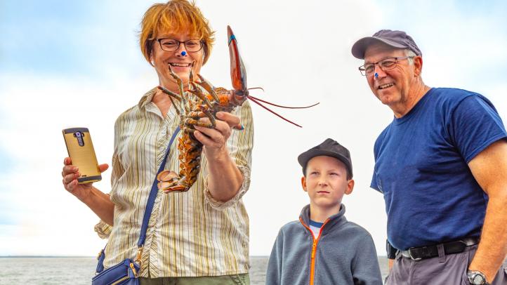 A person holding a lobster while two people look on. 