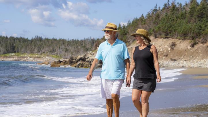 Two people walk holding hands on the beach in Cape Breton.
