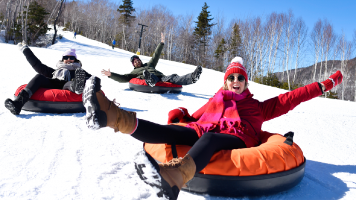 Three people on inflatable tubes sliding downhill at Destination Cape Smokey. 