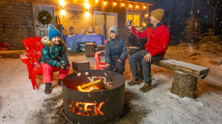 People sitting next to a fire at their Seek Wilderness accommodations. 