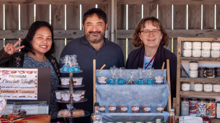 Three people working a stall at the Bellieau Cove Farmers Market. 