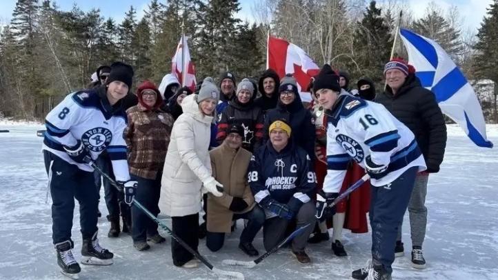 Minister Ritcey and ceremonial puck drop with hockey players and fans. It is an outdoor rink. 