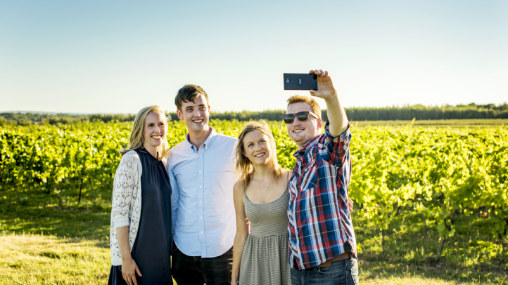 Four people in a field taking a selfie iwith crops growing in the background. 
