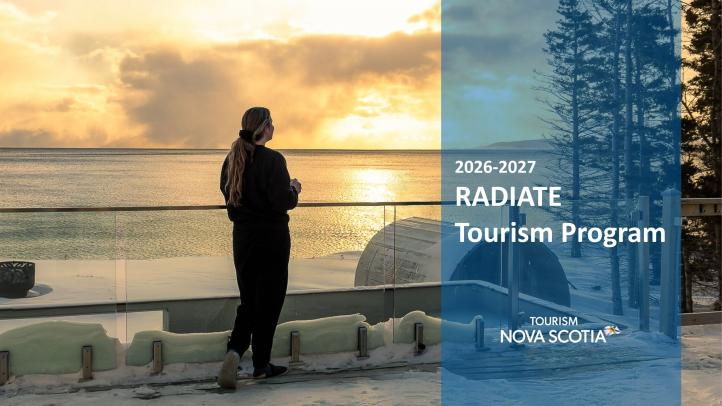 A person standing back to on a balcony holding a mug at sunset