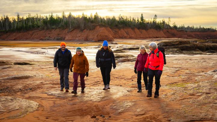 Five people waling in the mud behind a small cliff with trees