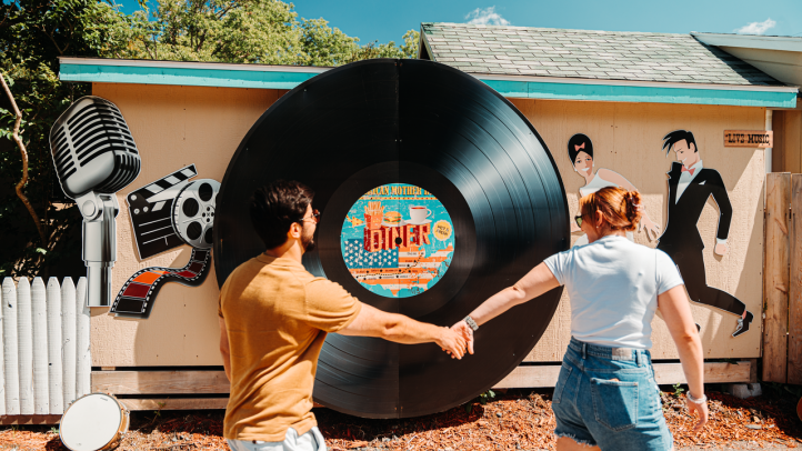 One person leading another by the hand in front of a large record on the side of a building. 