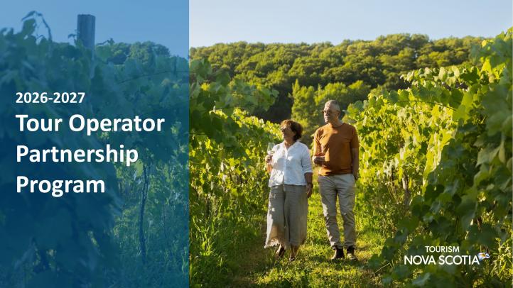 Two people walking through a green vineyard holding a glass of wine