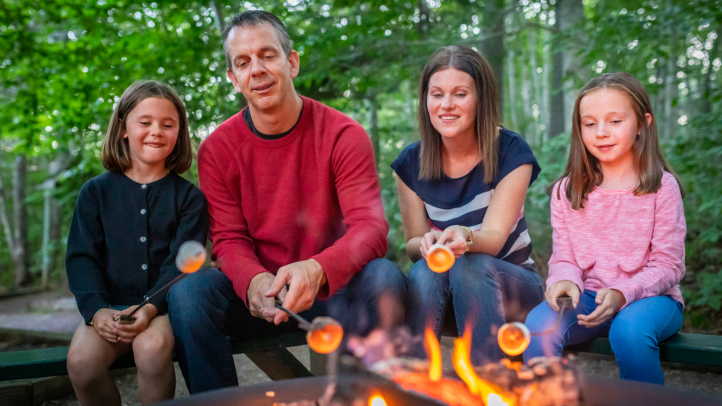 A family sitting at a campsite roasting marshmallows over a fire. 