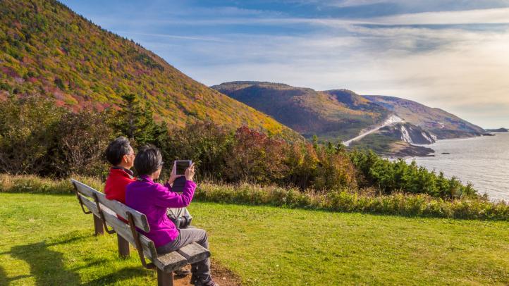 Two people sitting on a bench overlooking what ocean taking a phone using their phones