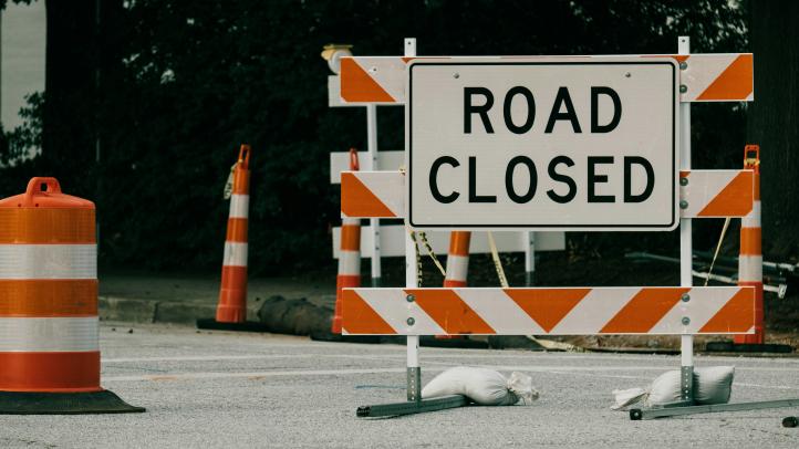 A road closed sign with pylons around it. 