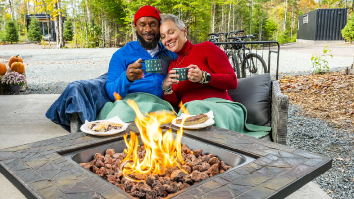 Two people sitting cuddling next to an outdoor fire table.
