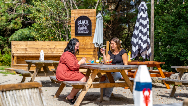Black Harbour Distillers in Hubbards. Two people are sitting at a picnic table enjoying a meal. 
