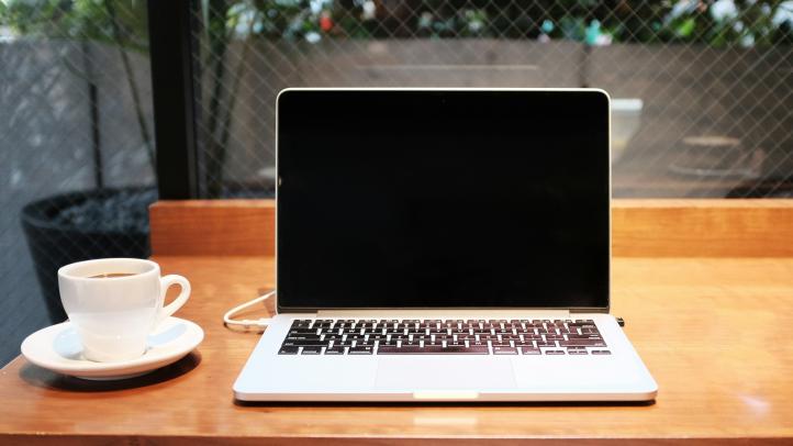 A laptop is open on a countertop. There is a coffee cup next to the computer. 