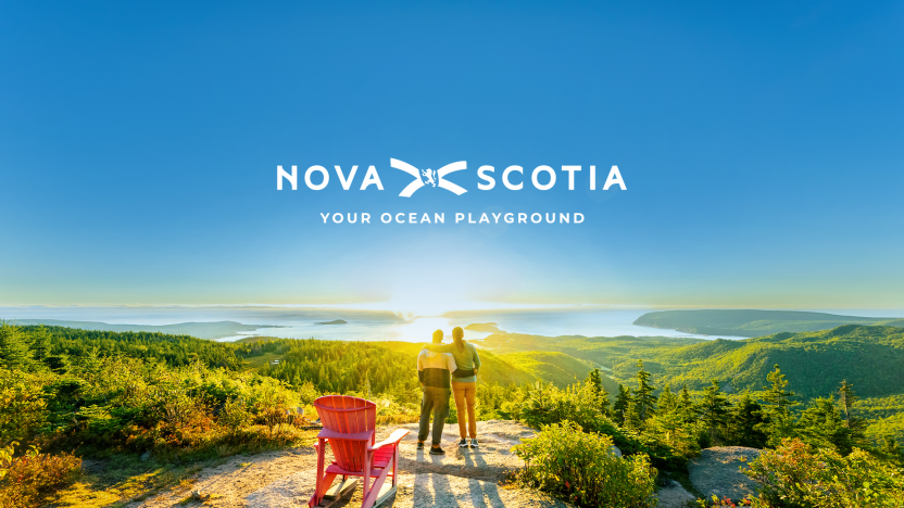 Two people at the top of Franey Trail in Cape Breton Highlands National Park. Text reads Nova Scotia Your Ocean Playground.