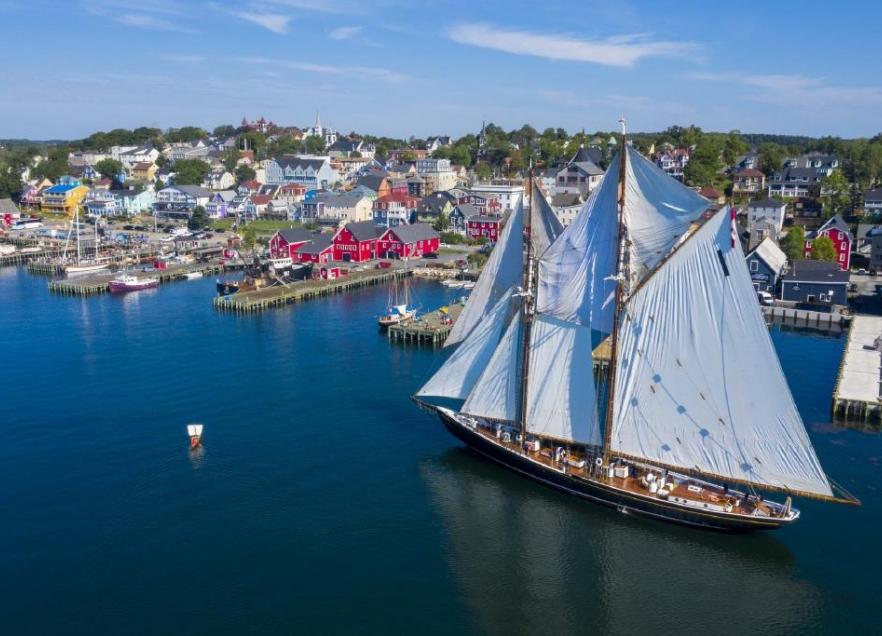 A drone captures the Bluenose II sailing ship coming in to the dock on the Lunenburg waterfront. The ships sails are full and the weather is sunny. 