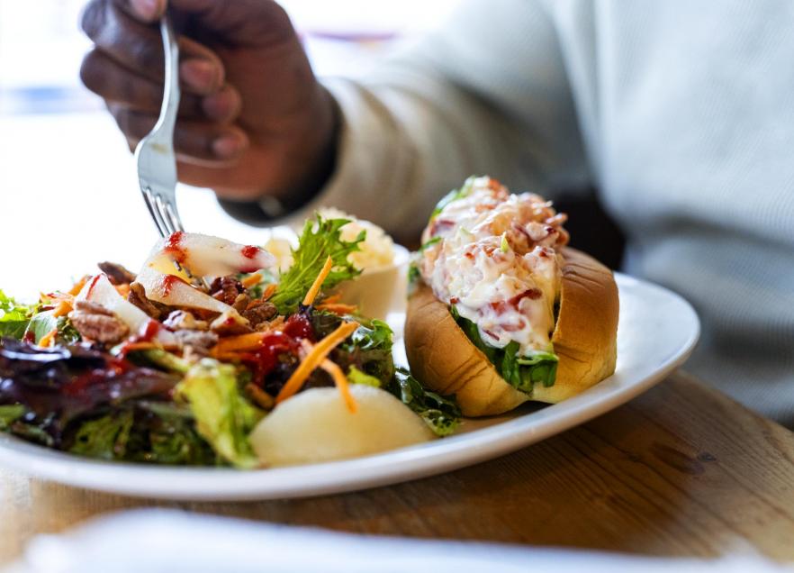 A person sitting at a table with fork in hand, digging into a lobster roll dinner. 