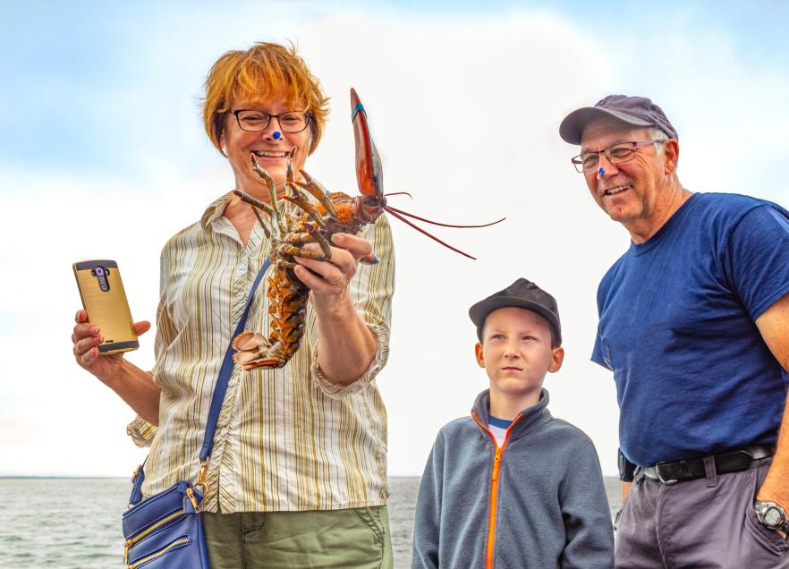 A person holding a lobster while two people look on. 