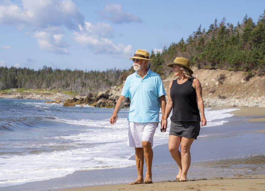 Two people walk holding hands on the beach in Cape Breton. 