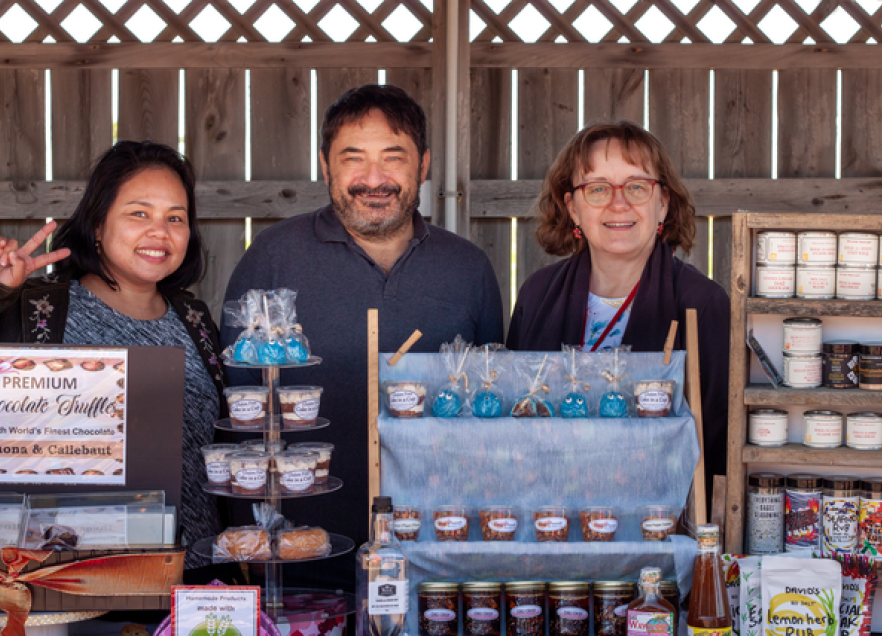 Three people working a stall at the Bellieau Cove Farmers Market. 