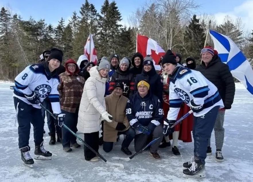 Minister Ritcey and ceremonial puck drop with hockey players and fans. It is an outdoor rink. 