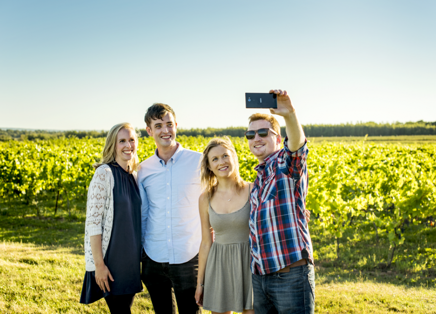 Four people in a field taking a selfie iwith crops growing in the background. 