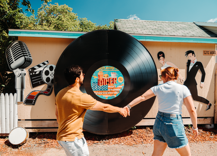 One person leading another by the hand in front of a large record on the side of a building. 